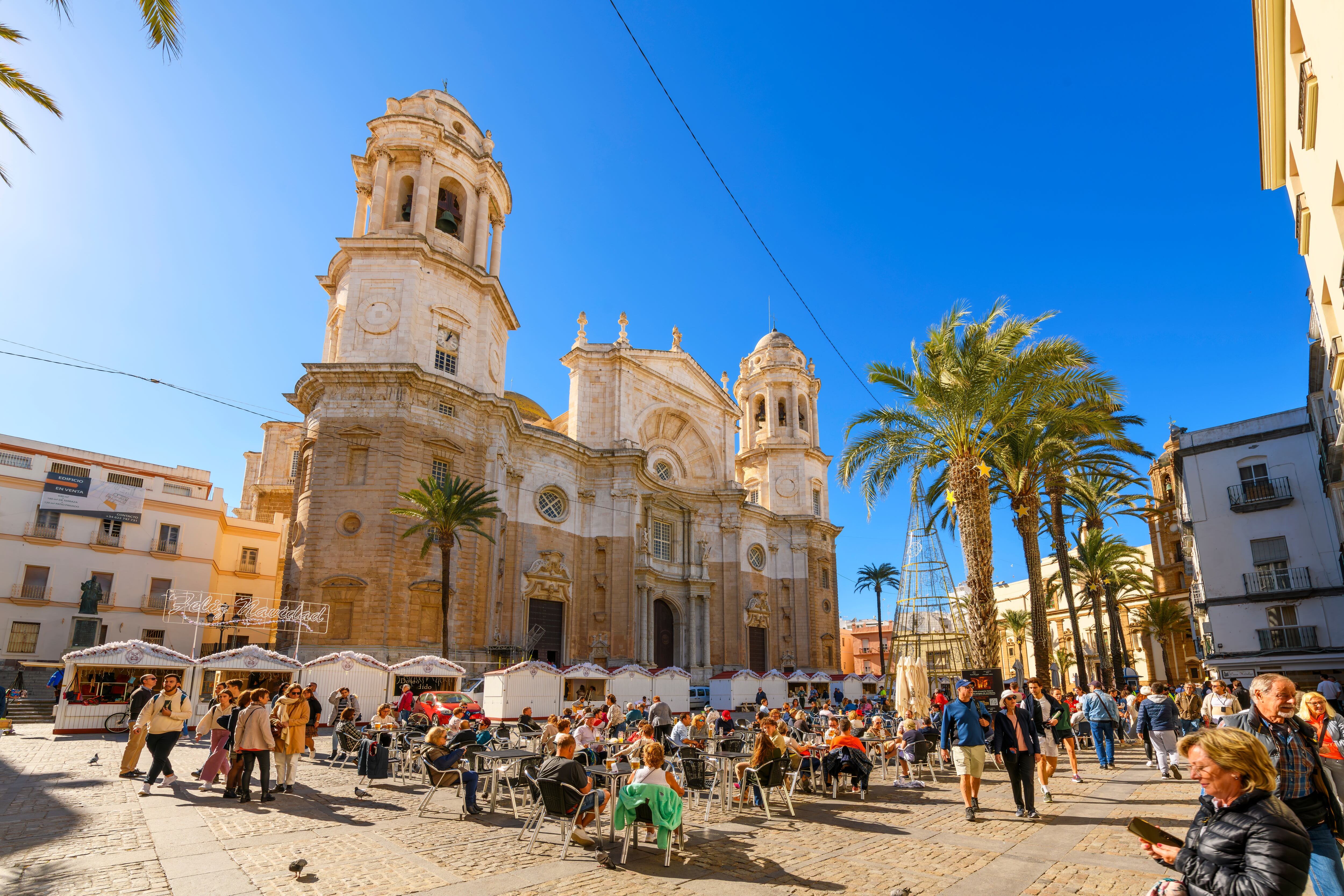 Los turistas comen al sol en la Plaza Catedral de la Santa Cruz de Cádiz, la principal Catedral del casco antiguo de la ciudad andaluza de Cádiz, España.