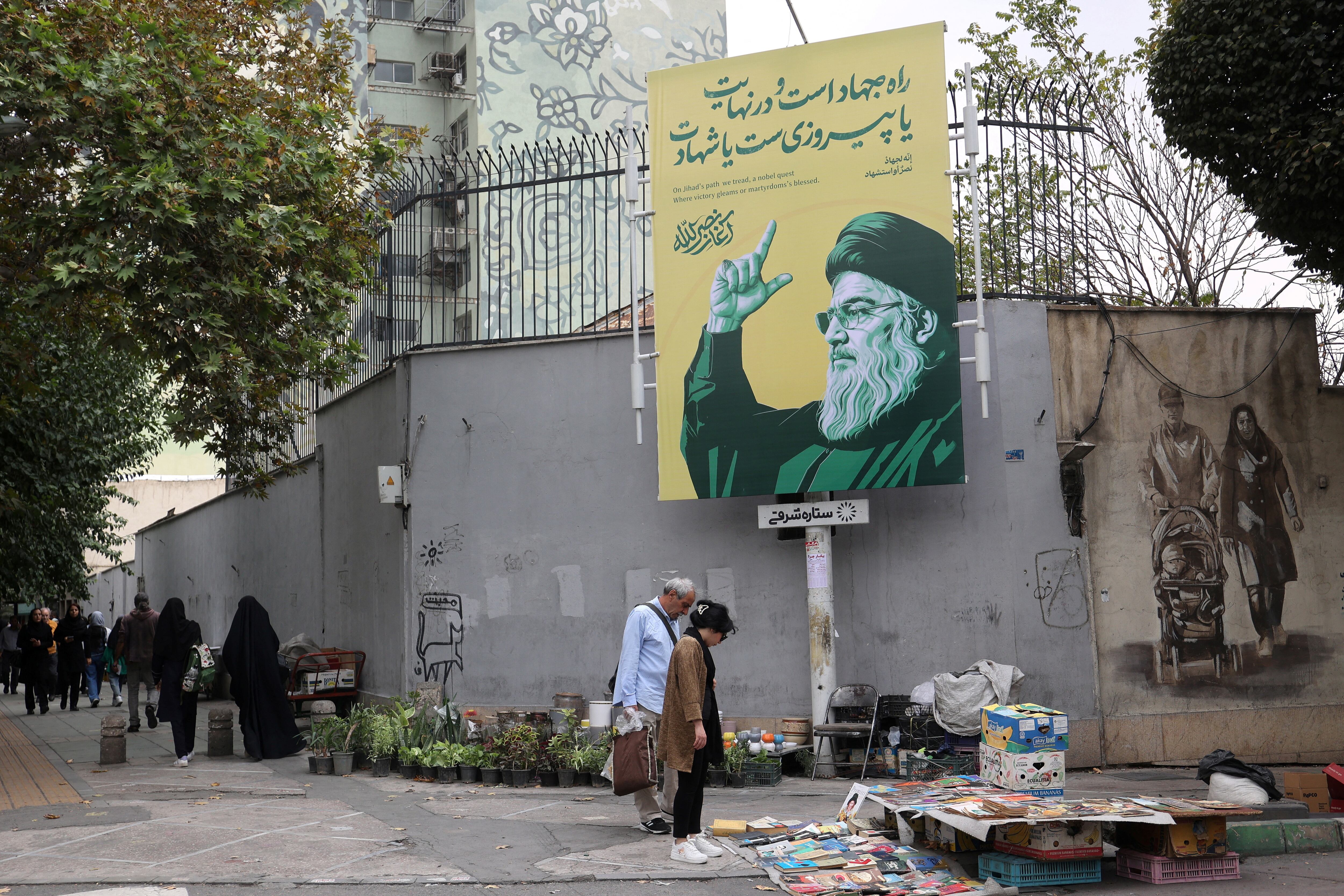 Varias personas se encuentran junto a una pancarta con una imagen del difunto líder de Hezbolá del Líbano, Sayyed Hassan Nasrallah, en una calle de Teherán (West Asia News Agency vía REUTERS)
