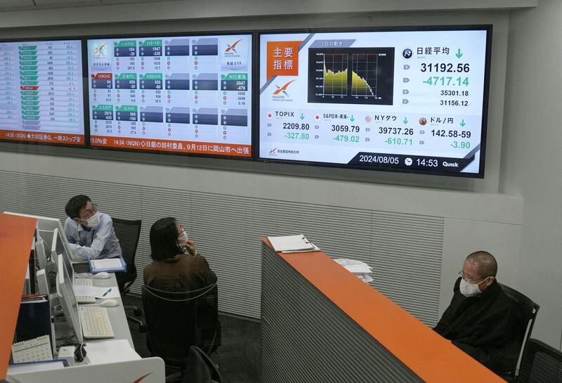 Empleados mirando monitores que muestran el promedio de acciones Nikkei de Japón, que ha tenido una caída récord en el precio de cierre, en la Bolsa de Valores de Nagoya (Reuters)