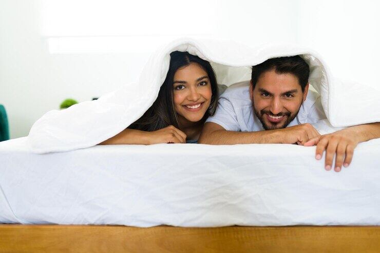 Una pareja feliz en la cama bajo la sábana - Bajo deseo sexual (Freepik)