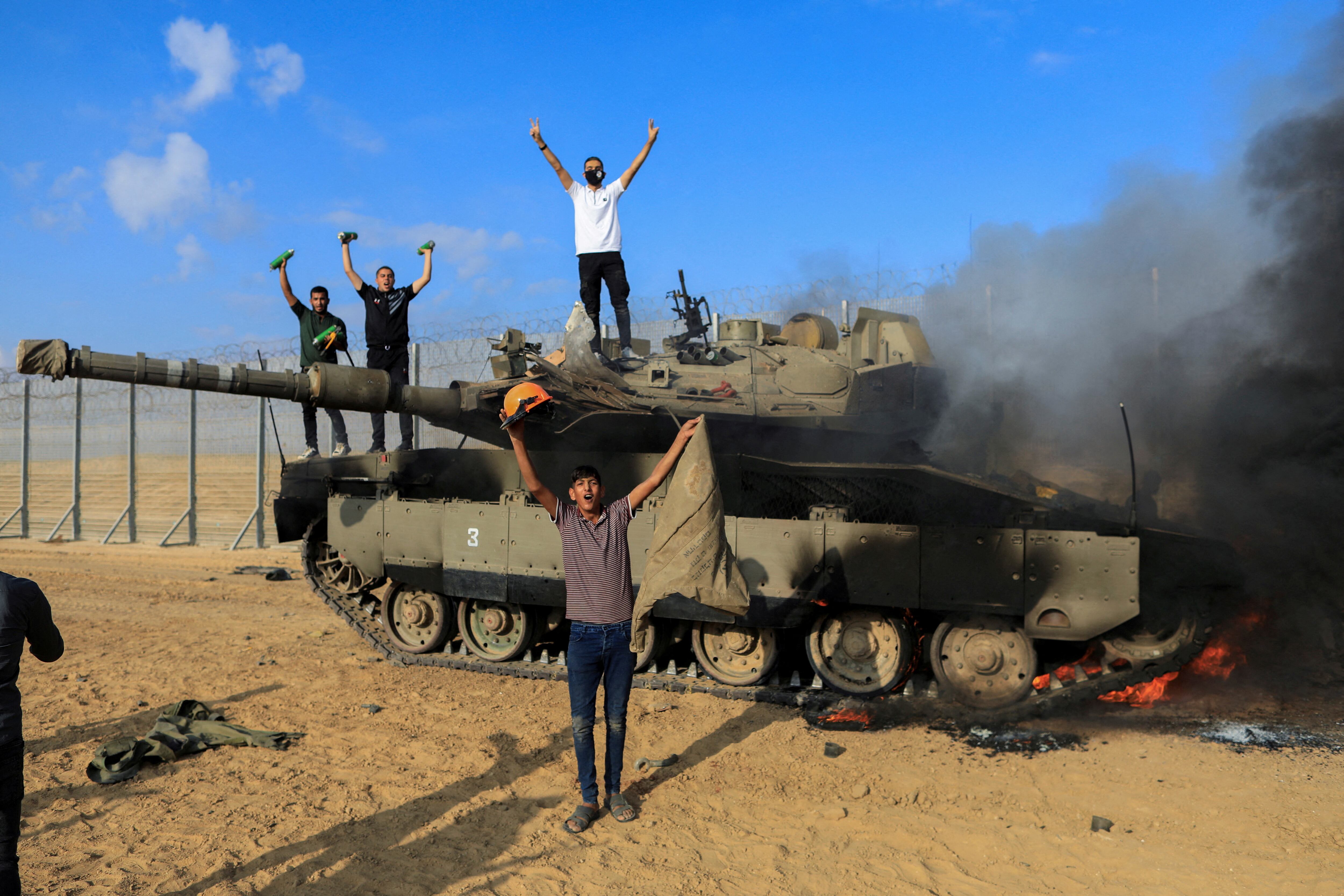 Un grupo de personas celebra mientras un vehículo militar israelí arde tras ser alcanzado por milicianos palestinos que se infiltraron en zonas del sur de Israel