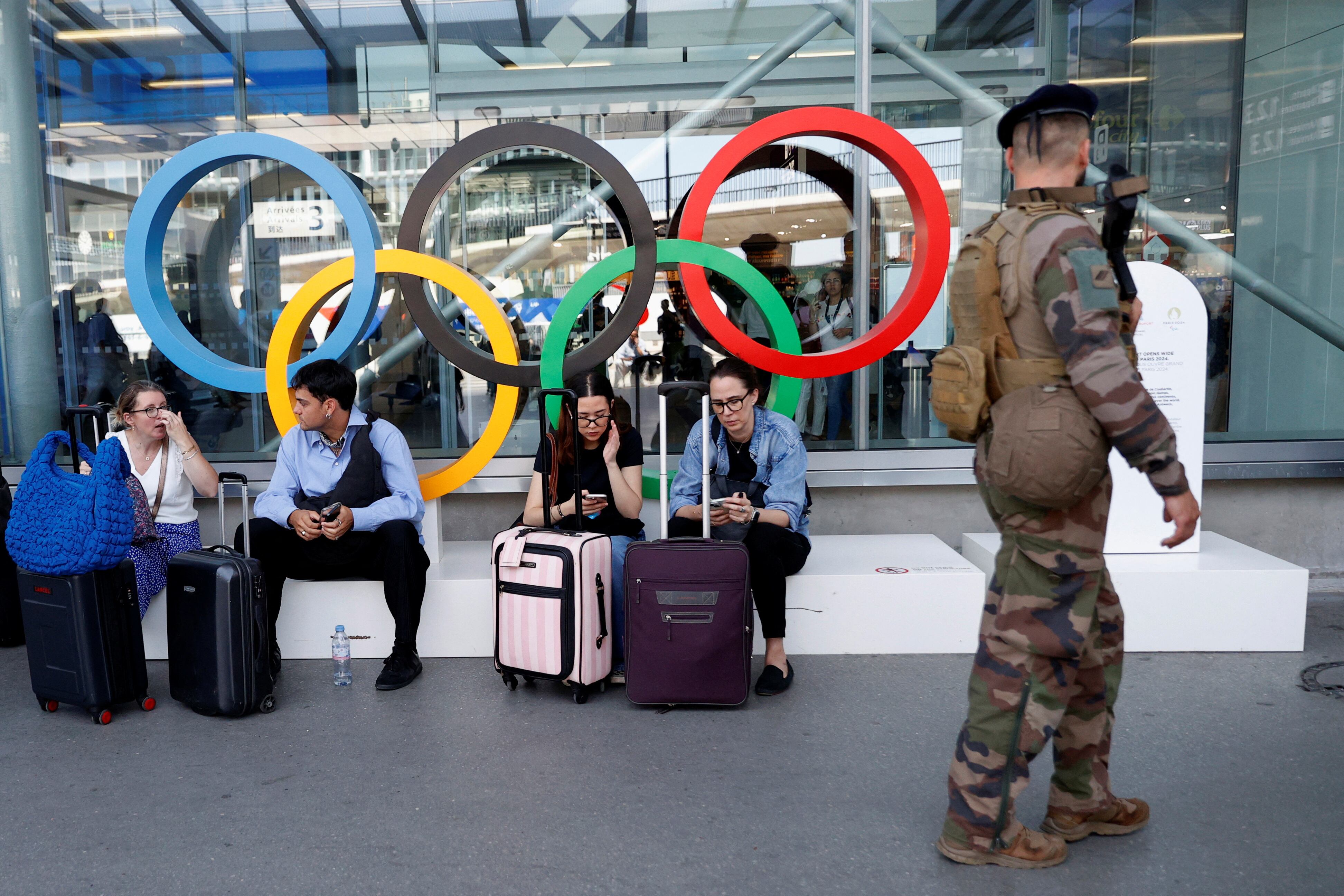 Un soldado francés pasa junto a los pasajeros sentados frente a los anillos olímpicos mientras patrullan fuera de la Terminal 3 del aeropuerto de Orly antes de los Juegos Olímpicos de París 2024 (REUTERS/Abdul Saboor)