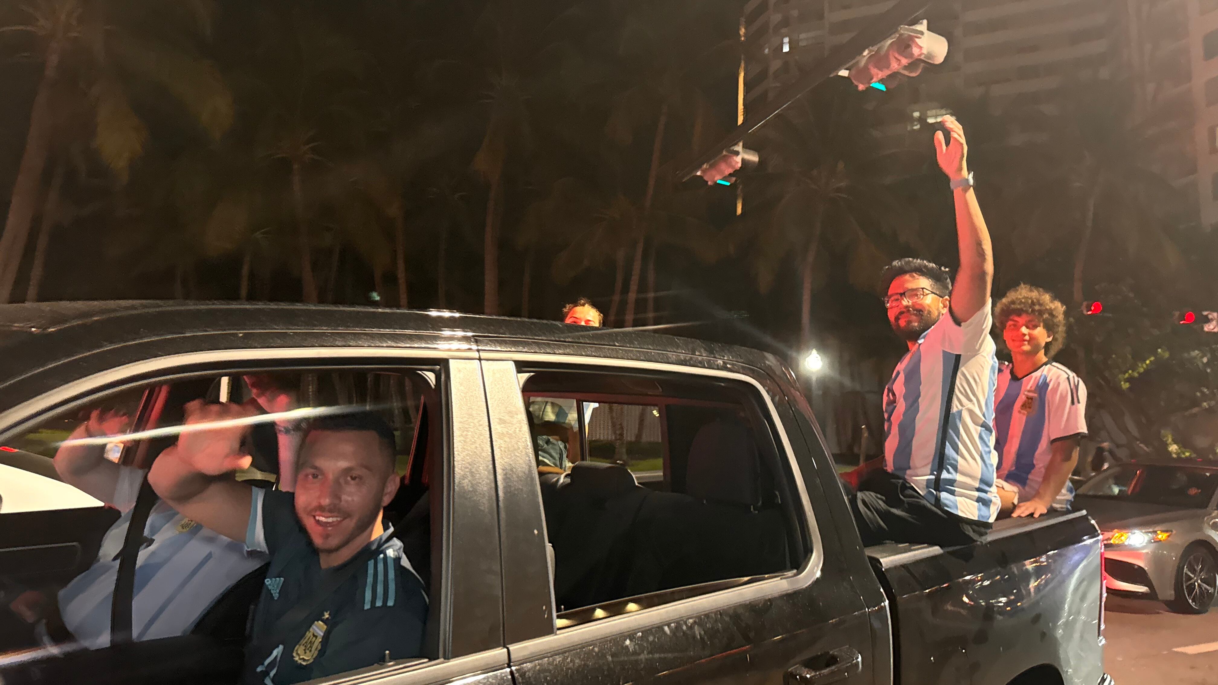 Una multitud de hinchas argentinos, vestidos con camisetas de la selección y agitando banderas celestes y blancas, celebra en las calles de Miami Beach durante la noche. La gente se muestra eufórica, tomando fotos y cantando, en una atmósfera festiva y llena de emoción tras la victoria de la Selección Argentina en la Copa América.