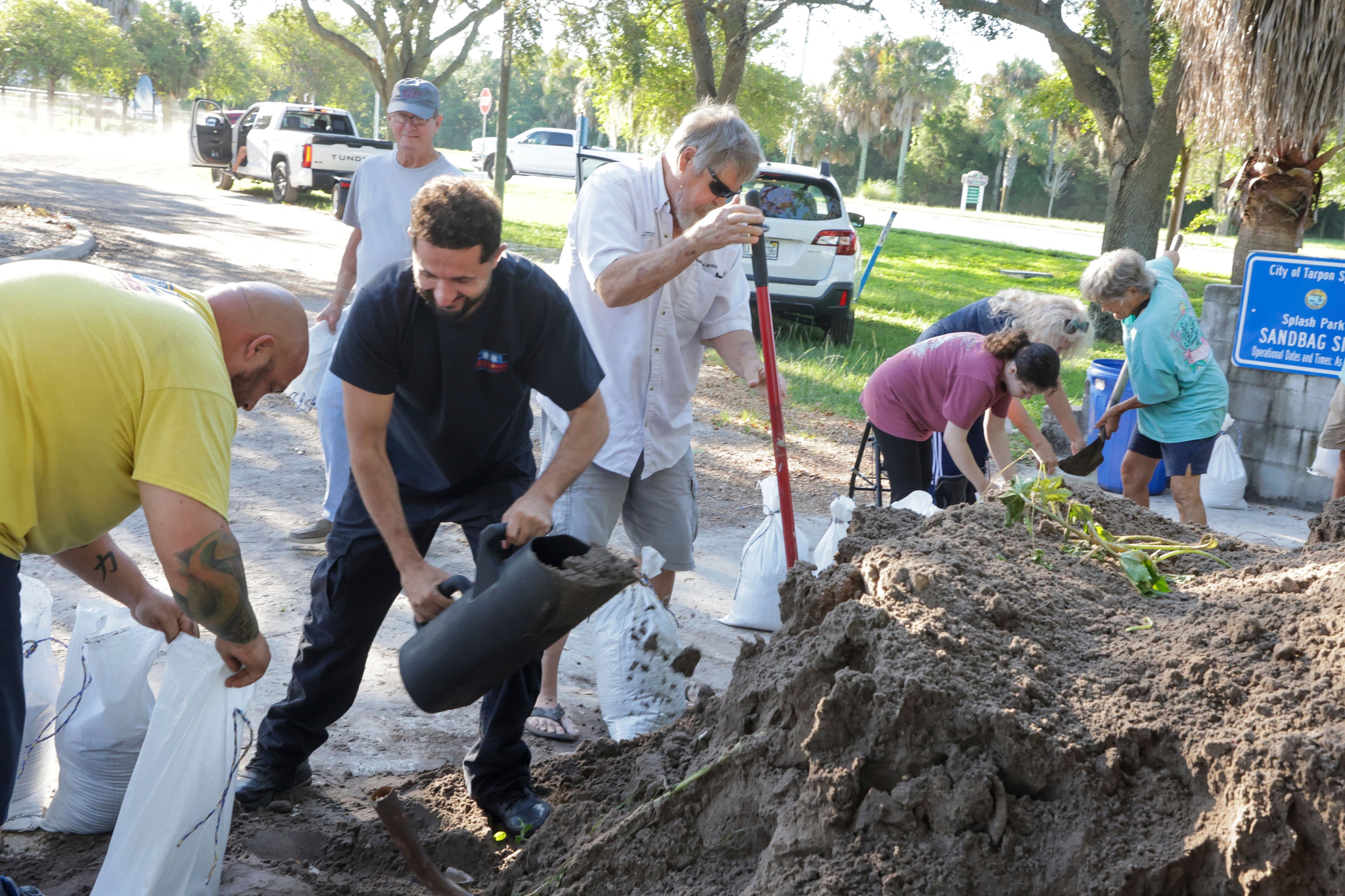 Varias personas llenan costales de arena en un emplazamiento público mientras los residentes preparan sus casas contra posibles inundaciones ante la cercanía de la tormenta tropical Helene, el 24 de septiembre de 2024, en Tarpon Springs, Florida. (Douglas R. Clifford/Tampa Bay Times vía AP)