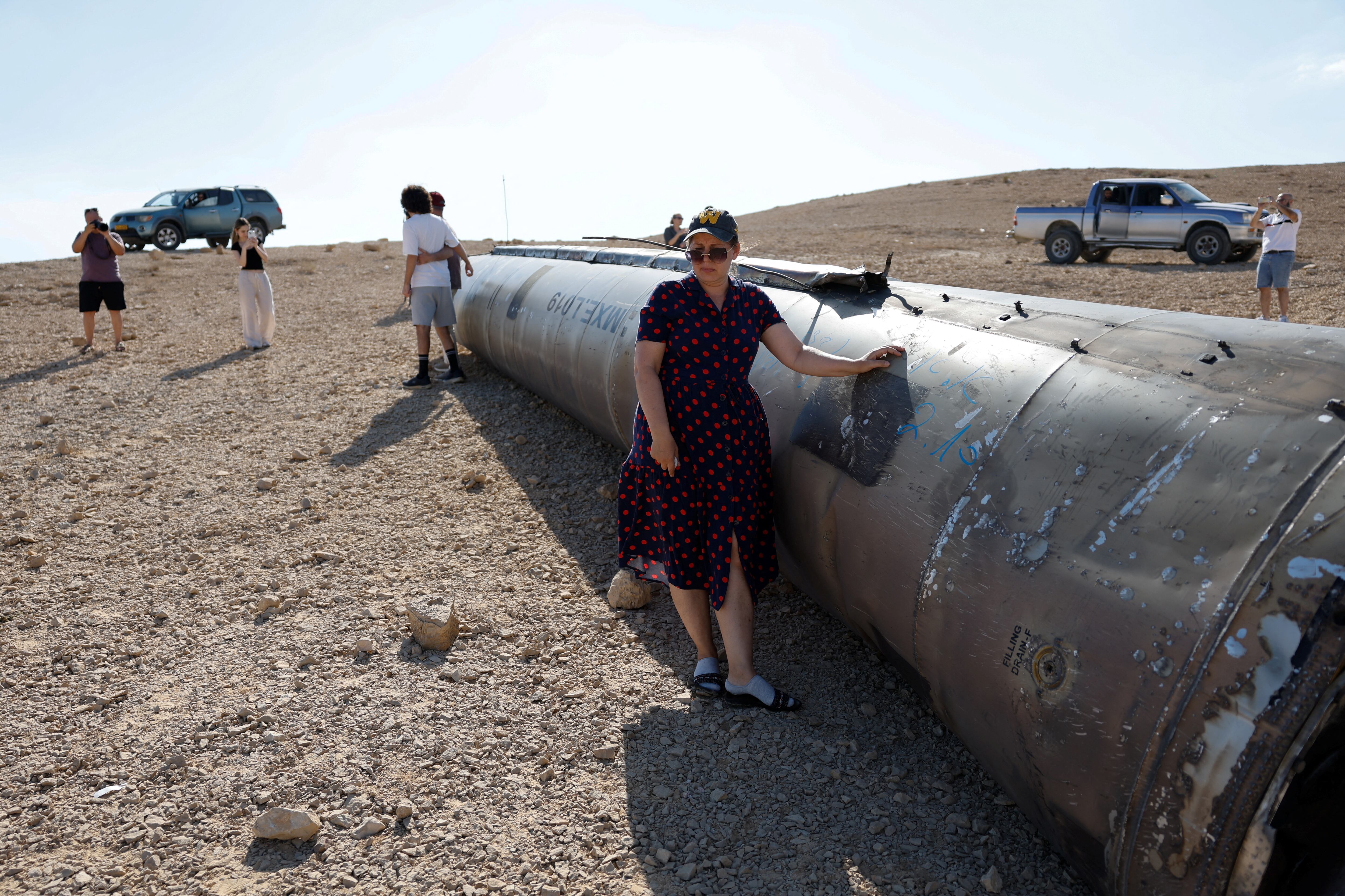 Varias personas posan junto a los restos aparentes de un misil balístico que yace en el desierto cerca de la ciudad meridional de Arad, Israel. (REUTERS/Amir Cohen)