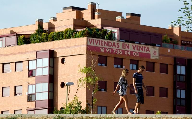 Una pareja paseando por delante de un bloque de pisos con un cartel de "Se vende" en una nueva zona residencial de Madrid. REUTERS/Paul Hanna