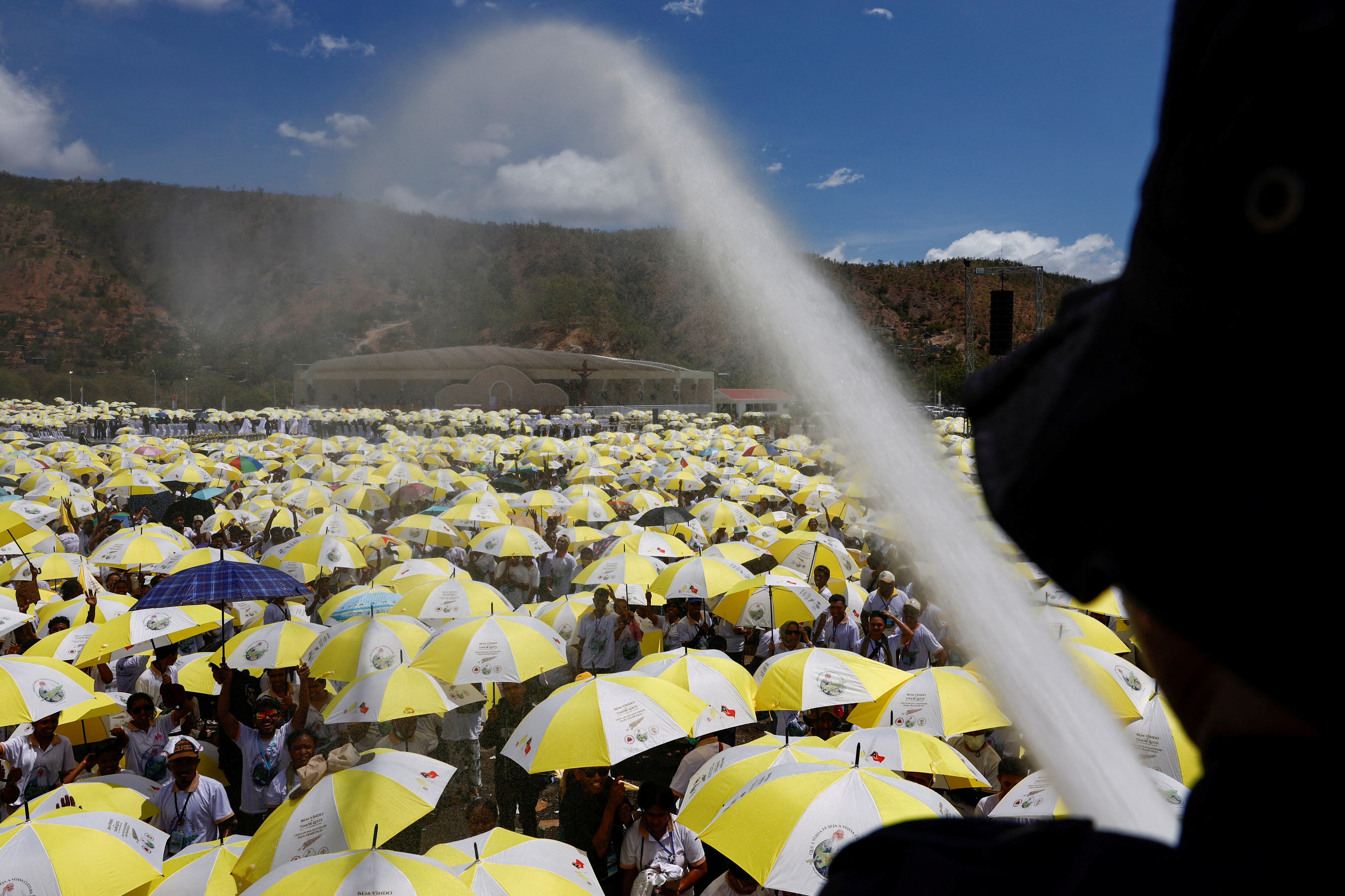 Un bombero rocía agua sobre fieles católicos reunidos para una Santa Misa con el Papa Francisco.